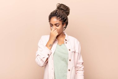 Genç afro kadın iğreniyor, kötü ve nahoş bir koku duymamak için burnunu tutuyor.