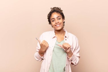 Genç afro kadın neşeyle gülümsüyor ve yan taraftaki fotokopi alanını gösteriyor, mutlu ve tatmin olmuş hissediyor.