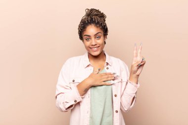 Genç afro kadın mutlu, kendinden emin ve güvenilir görünüyor, gülümsüyor ve zafer işareti gösteriyor, olumlu bir tavırla.