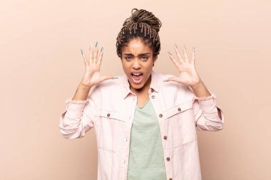 Genç afro kadın panik ya da öfke içinde bağırıyor, şok olmuş, korkmuş ya da öfkeli, elleri başının yanında.