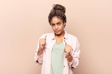 Genç afro kadın kendinden emin, sinirli, güçlü ve agresif görünüyor. Yumrukları boks pozisyonunda dövüşmeye hazır.