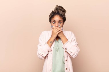 Genç afro kadın şok olmuş, şaşırmış bir ifadeyle ağzını kapatıyor, sır saklıyor ya da 