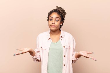 Genç afro kadın şaşkın ve kafası karışık, doğru cevap ya da karardan emin değil, bir seçim yapmaya çalışıyor.