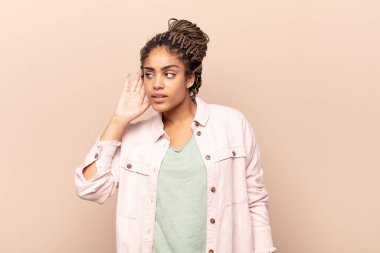 Genç afro kadın ciddi ve meraklı görünüyor, dinliyor, gizli bir konuşma veya dedikodu duymaya çalışıyor, kulak misafiri oluyor.