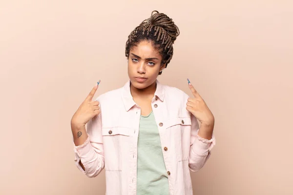 young afro woman with a bad attitude looking proud and aggressive, pointing upwards or making fun sign with hands