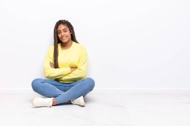 Kameraya çapraz kollu gülümseyen genç afro kadın ve mutlu, kendinden emin, tatmin olmuş bir ifade, yan görüş.