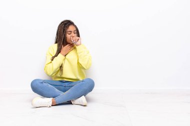 Boğazı ağrıyan ve grip belirtileri gösteren, ağzı kapalı öksüren genç afro bir kadın.