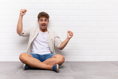 Genç adam muzaffer bir şekilde bağırıyor, heyecanlı, mutlu ve şaşırmış görünüyor.