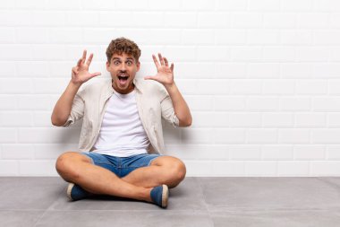 Genç adam panik ya da öfke içinde bağırıyor. Şok olmuş, korkmuş ya da öfkeli. Elleri başının yanında.