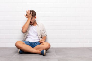 young man raising palm to forehead thinking oops, after making a stupid mistake or remembering, feeling dumb