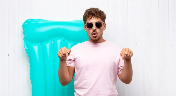 young man with open mouth pointing downwards with both hands, looking shocked, amazed and surprised. holidays concept