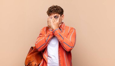 Delikanlı korkmuş ya da utanmış hissediyor. Gözleri yarı kapalı elleriyle dikizliyor ya da dikizliyor. öğrenci konsepti