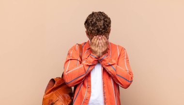 Genç adam üzgün, hayal kırıklığına uğramış, gergin ve depresif, iki eliyle yüzünü kaplayan, ağlayan. öğrenci konsepti