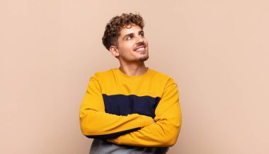 Genç adam mutlu, gururlu ve umutlu, merak ediyor ya da düşünüyor, çapraz kollarla uzayı taklit ediyor.