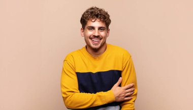 Genç adam utangaç ve neşeli bir şekilde gülüyor, arkadaş canlısı ve olumlu ama güvensiz bir tavırla.