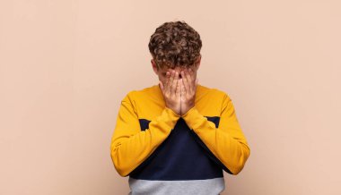 Genç adam üzgün, hayal kırıklığına uğramış, gergin ve depresif, iki eliyle yüzünü kaplayan, ağlayan