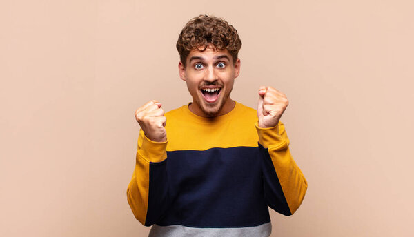 Молодой человек чувствует себя шокированным, взволнованным и счастливым, смеясь и празднуя успех, говоря вау!