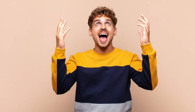 Genç adam mutlu, şaşkın, şanslı ve şaşırmış hissediyor, zaferi kutluyor, iki eli havada.