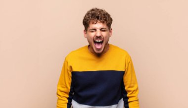 Genç adam agresif bir şekilde bağırıyor, çok kızgın, hayal kırıklığına uğramış, öfkeli ya da sinirli görünüyor.