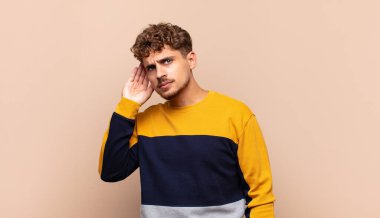 Genç adam ciddi ve meraklı görünüyor, dinliyor, gizli bir konuşma ya da dedikodu duymaya çalışıyor, gizlice dinliyor.