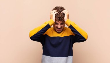 Genç adam kendini stresli ve hayal kırıklığına uğramış hissediyor, ellerinizi havaya kaldırıyor, yorgun, mutsuz ve migren ağrısı çekiyor.