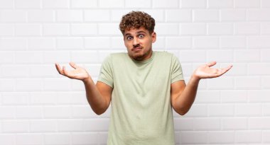 Genç adam şaşkın ve şaşkın hissediyor, şüpheci, farklı seçenekleri tartıyor veya komik bir ifadeyle seçiyor.