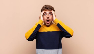 Genç adam mutsuz, korkmuş ya da endişeli görünüyor, ağzı sonuna kadar açık ve iki kulağını da elleriyle kapatıyor.