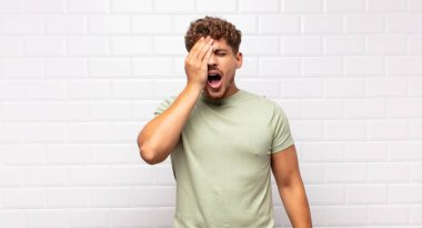 Genç adam uykulu, sıkılmış ve esniyor, baş ağrısı ve yüzünün yarısını kaplayan bir elle.