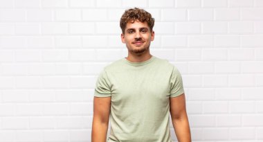 Genç adam pozitif ve kendinden emin bir şekilde gülümsüyor, tatmin olmuş, arkadaş canlısı ve mutlu görünüyor.