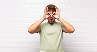 Genç adam şaşkın, şaşırmış ve şaşırmış hissediyor. Elinde şaşkın, inançsız bir bakışla gözlük tutuyor.