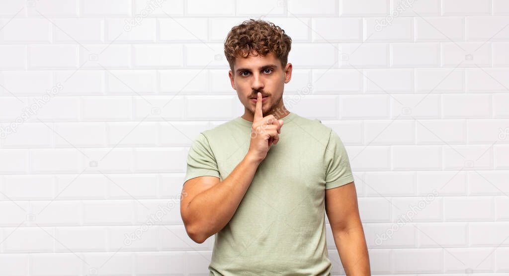 young man looking serious and cross with finger pressed to lips demanding silence or quiet, keeping a secret