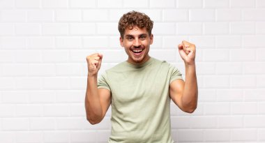 Genç adam mutlu, şaşırmış ve gururlu, bağırıyor ve başarıyı büyük bir gülümsemeyle kutluyor.