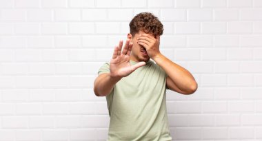 Genç adam yüzünü eliyle kapatıyor ve kamerayı durdurmak için diğer elini öne koyuyor, fotoğraf ya da resimleri reddediyor.