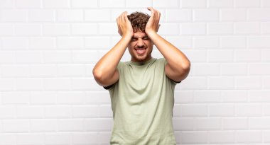 Genç adam stresli ve endişeli, depresif ve hayal kırıklığına uğramış hissediyor, iki elini de başa kaldırıyor.
