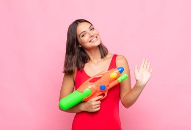 Genç ve güzel bir kadın mutlu ve neşeli bir şekilde gülümsüyor, el sallıyor, sizi selamlıyor ve selamlıyor, ya da veda ediyor. yaz konsepti