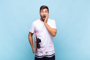 Genç adam şok olmuş ve korkmuş hissediyor, ağzı açık ve elleri yanaklarında korkmuş görünüyor.