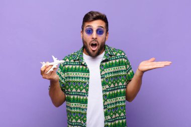 Genç adam şaşırmış ve şok olmuş görünüyor, çenesi düşmüş ve eli açık bir obje tutuyor. tatil kavramı