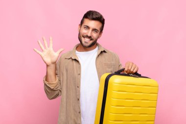 Genç adam gülümsüyor ve arkadaş canlısı görünüyor. Beş ya da beş numarayı gösteriyor. Elleri önde, geriye doğru sayıyor. tatil kavramı