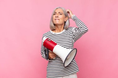 Orta yaşlı kadın şaşkın ve kafası karışmış hissediyor, kafasını kaşıyor ve megafonla yan tarafa bakıyor.