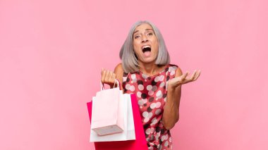 Orta yaşlı kadın umutsuz ve hayal kırıklığına uğramış görünüyor, stresli, mutsuz ve sinirli, alışveriş torbalarıyla bağırıyor ve çığlık atıyor.