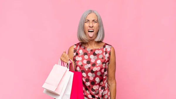 中年の女性はうんざりしていらいらして舌を出し買い物袋で何か嫌なことや幸運を嫌い — ストック写真