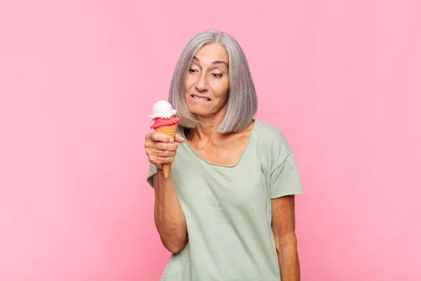 middle age woman looking puzzled and confused, biting lip with a nervous gesture, not knowing the answer to the problem having an ice cream