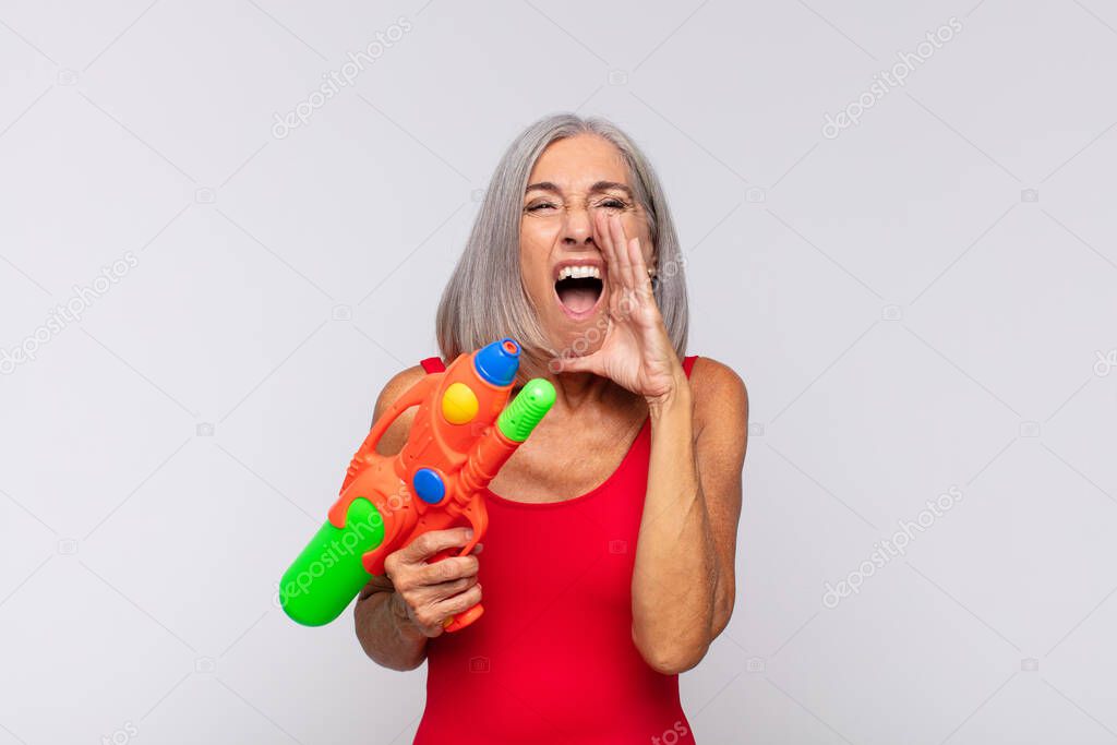 middle age woman feeling happy, excited and positive, giving a big shout out with hands next to mouth, calling out with a water gun
