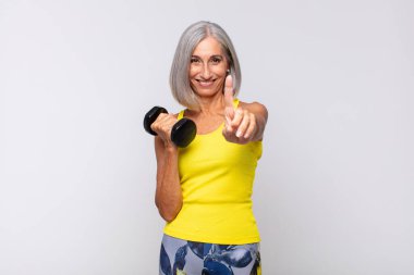 Orta yaşlı bir kadın gururla gülümsüyor ve gururla bir numaralı pozunu veriyor, kendini lider gibi hissediyor. fitness konsepti