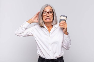 Orta yaşlı bir kadın stresli, endişeli, endişeli ya da korkmuş, elleri başının üstünde, hata kahve konseptiyle panikliyor.