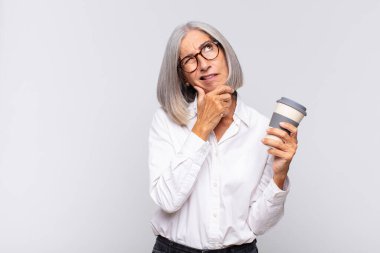 Orta yaşlı kadın düşünüyor, şüpheci ve şaşkın hissediyor, farklı seçenekleri var, kahve konsepti yapmak için hangi kararı vereceğini merak ediyor.