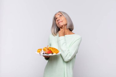 Orta yaşlı bir kadın mutlu bir şekilde gülümsüyor ve hayal kuruyor ya da şüphe ediyor, yana bakıyor. kahvaltı kavramı