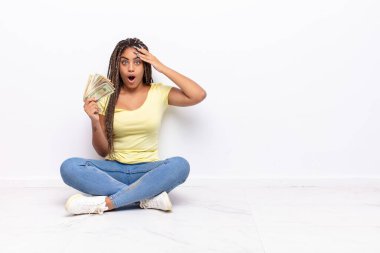 Genç afro kadın mutlu, şaşkın ve şaşırmış görünüyor, gülümsüyor ve inanılmaz ve inanılmaz iyi haberleri fark ediyor. para kavramı