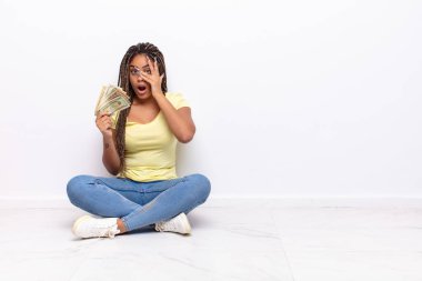 Genç afro kadın şok olmuş, korkmuş ya da korkmuş görünüyordu. Yüzü elle kaplıydı ve parmaklarının arasından bakıyordu. para kavramı