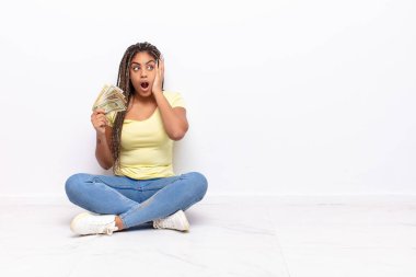 Genç afro kadın mutlu, heyecanlı ve şaşırmış hissediyor, iki eli yüzü yana bakıyor. para kavramı